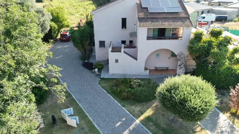 L’allée de gravier clair qui traverse le jardin jusqu’à la maison